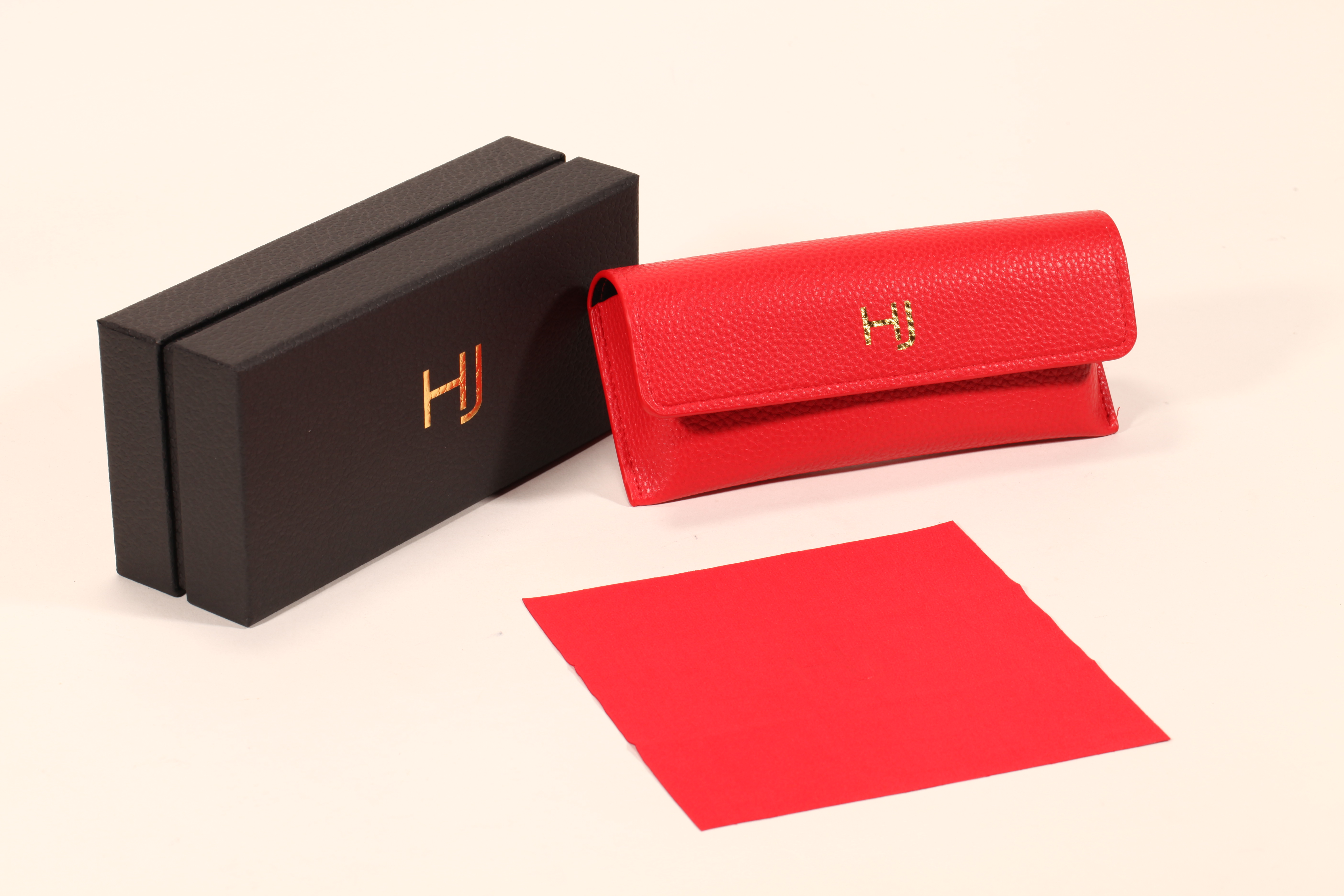 A stylish eyeglass case set features a black paper box, a red soft eyeglass case, and a red cleaning cloth.