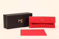 A stylish eyeglass case set features a black paper box, a red soft eyeglass case, and a red cleaning cloth.