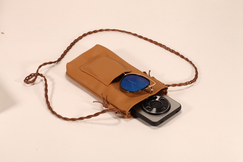 Este es un bolso de cuero marrón. Tiene un cordón y puede almacenar móviles y lentes de sol. Es práctico y elegante.