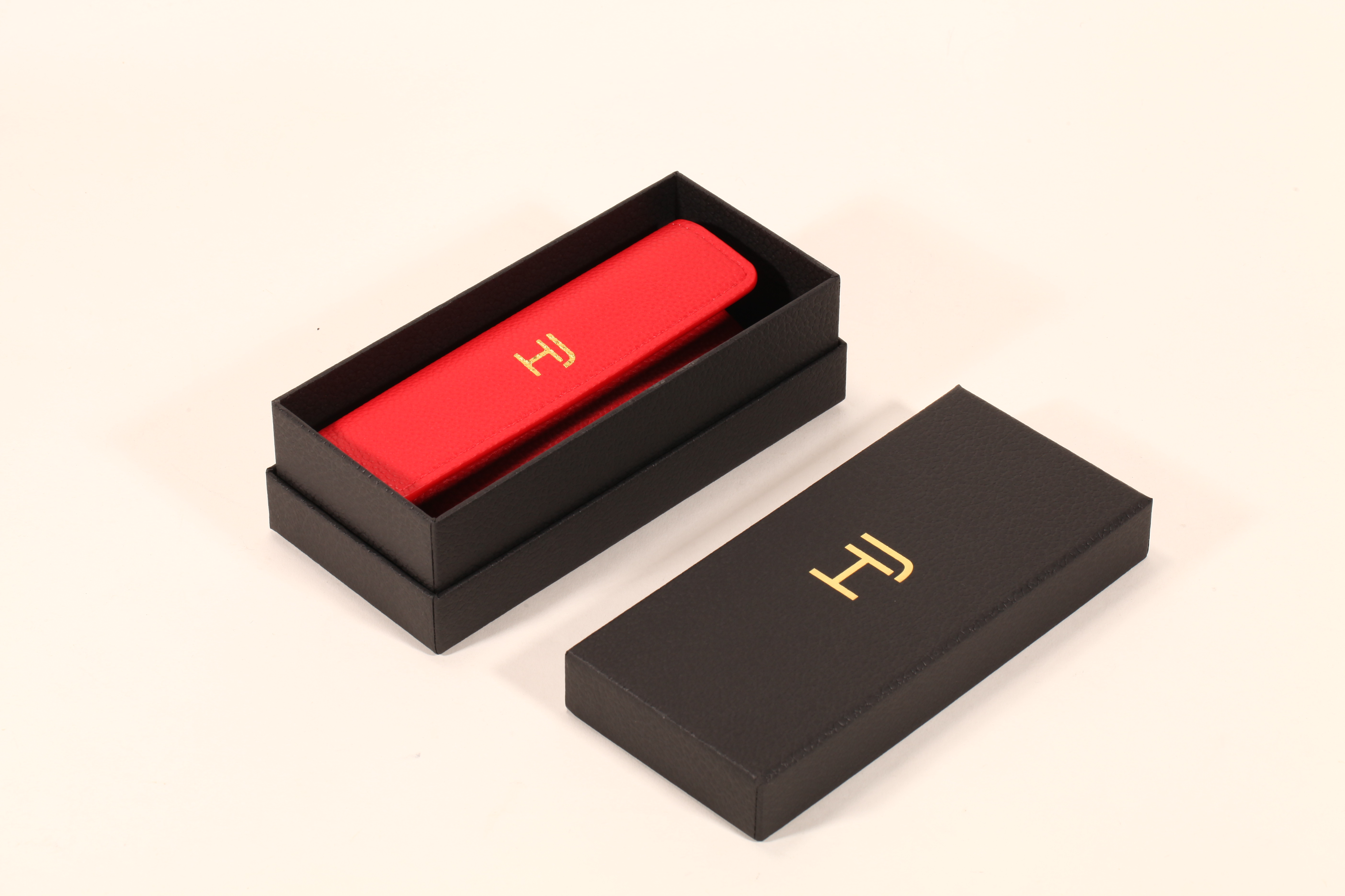 A stylish eyeglass case set features a black paper box, a red soft eyeglass case, and a red cleaning cloth.