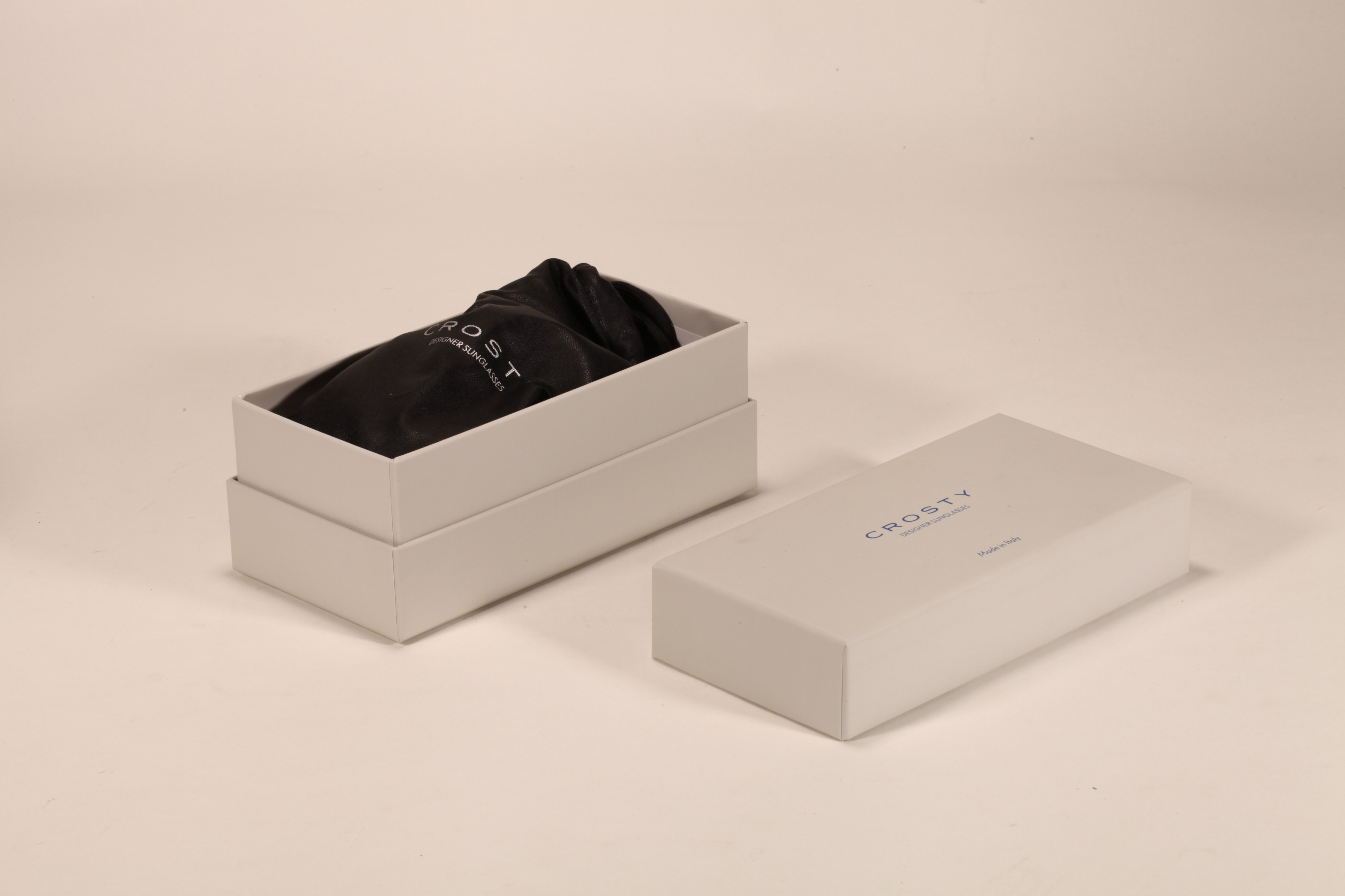 Este set de accesorios para gafas de la marca Crosty incluye una bolsa negra, un estuche blanco y unas gafas de sol de diseño elegante.
