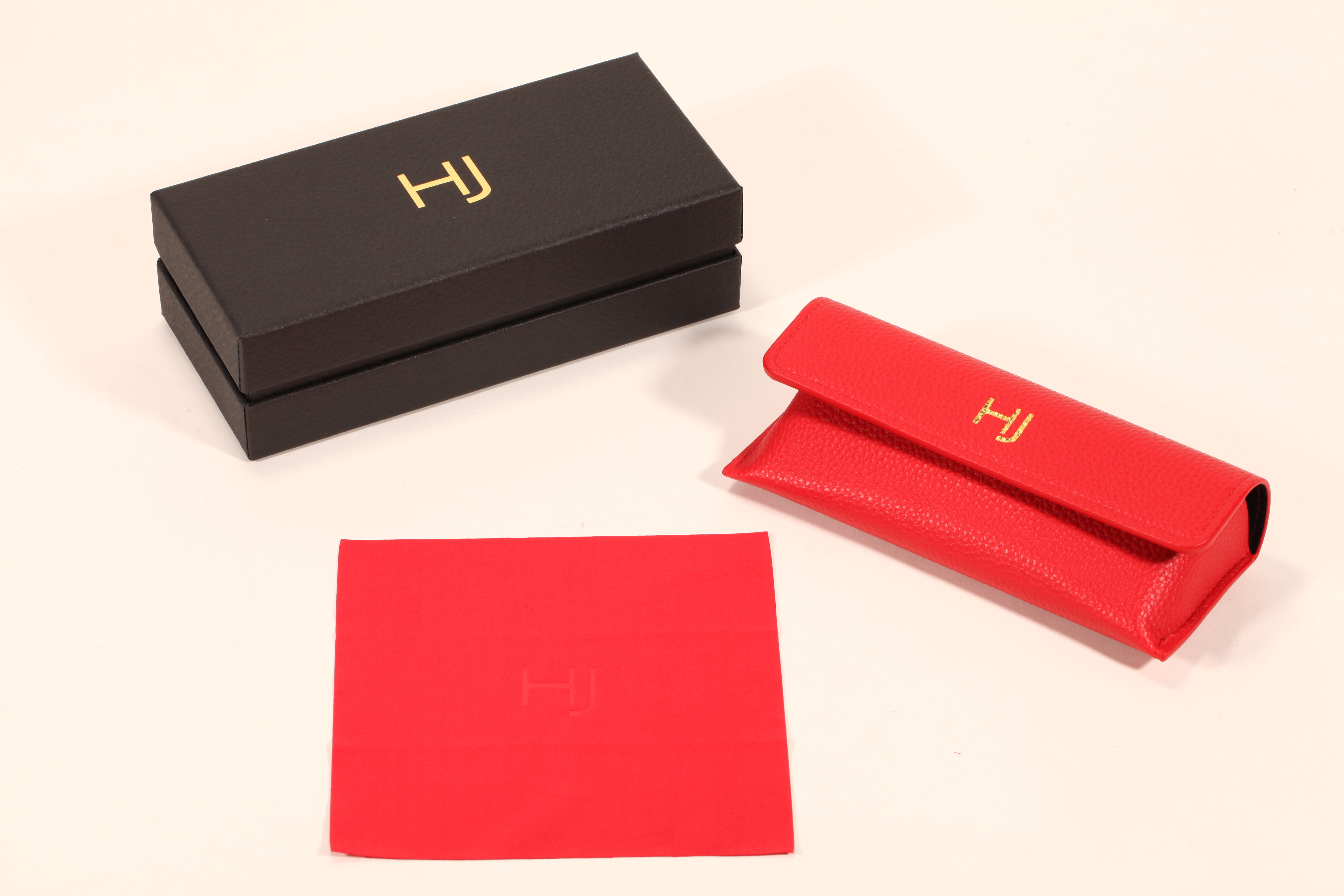 A stylish eyeglass case set features a black paper box, a red soft eyeglass case, and a red cleaning cloth.