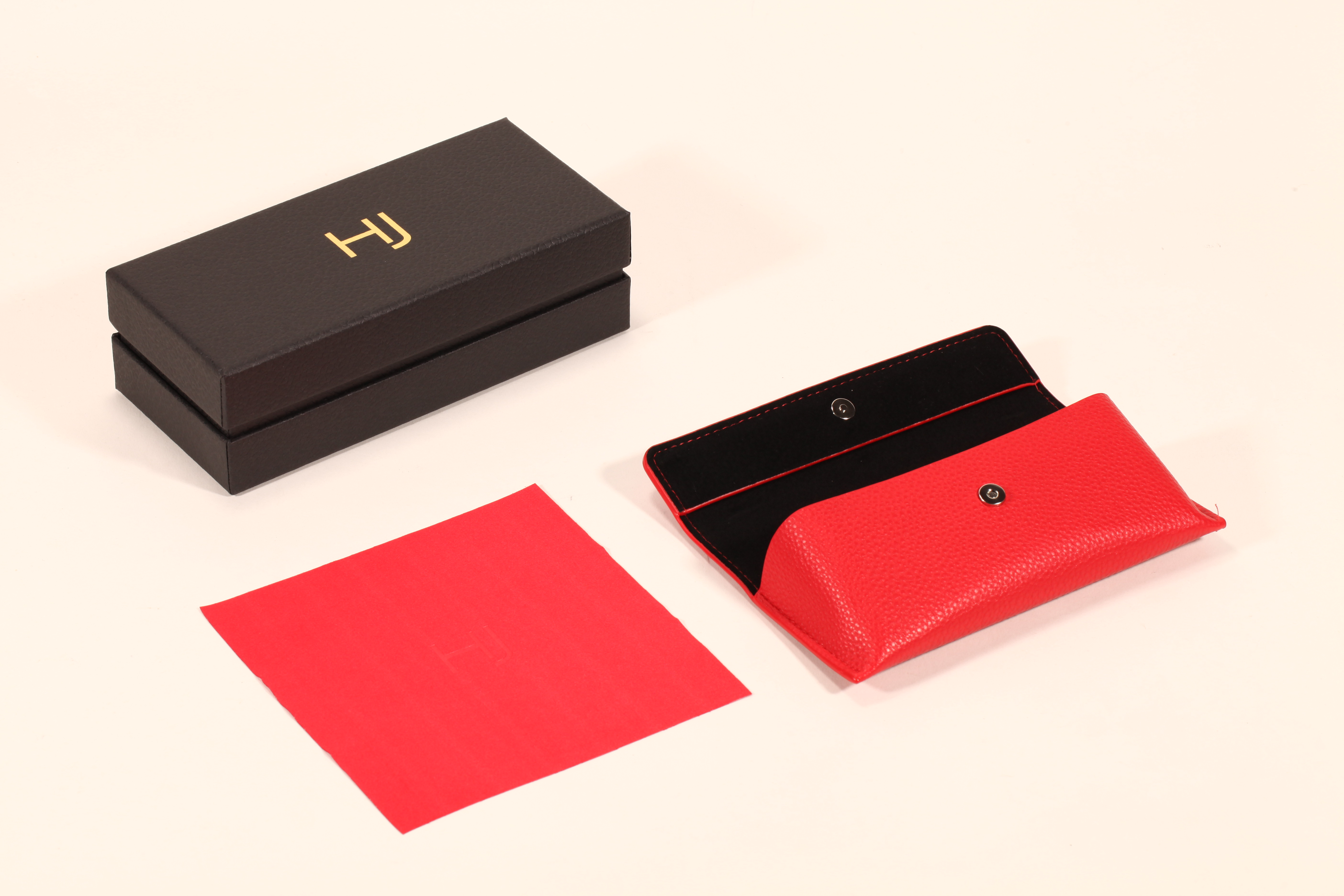 A stylish eyeglass case set features a black paper box, a red soft eyeglass case, and a red cleaning cloth.