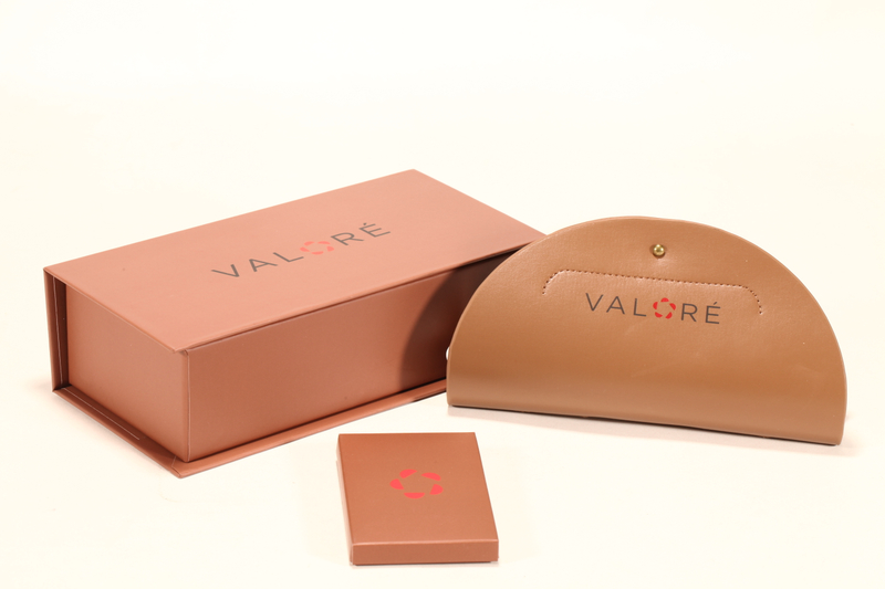 This Valoré eyewear set features a pink box, a tan semi-circular leather case (with gold snap), and a small square card. It exhibits elegant minimalist design, premium texture, and consistent branding
