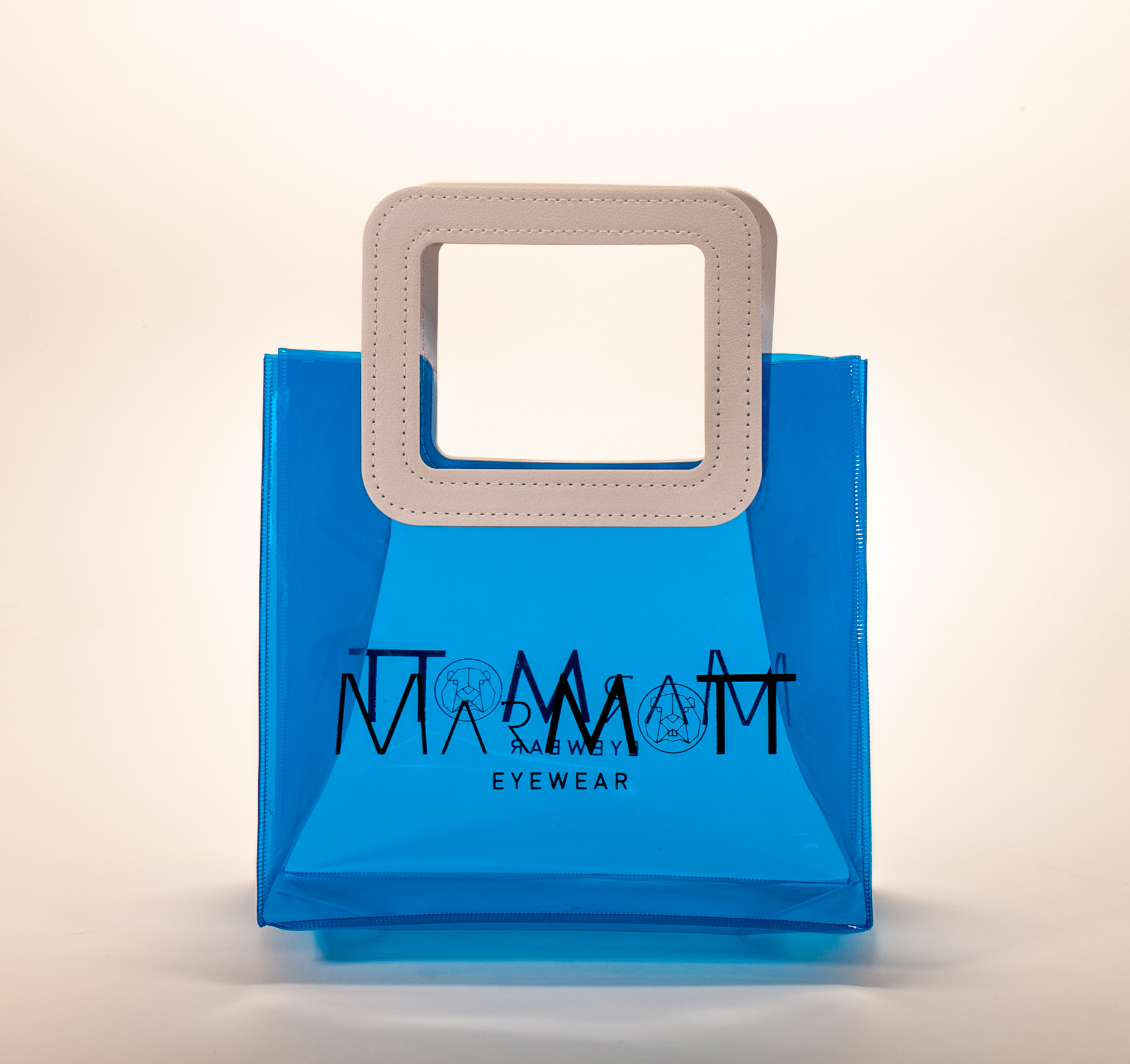 Three translucent bags in green, pink, and blue feature white square handles. The front displays the black text "MARMOTT EYEWEAR".